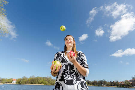 A slender young woman juggling with three crunchy applesの写真素材