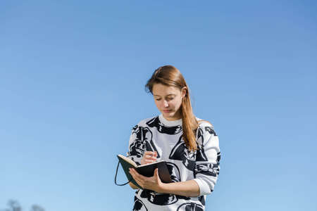 Young woman writes something in a notebook during nice weatherの写真素材