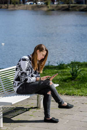 A woman reading something on her tablet on a bench in the park in the sunshineの写真素材