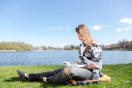 A woman reads a book in a park during nice weatherの写真素材