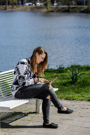Young woman sitting on a beautiful day in the park on a bench with a Tabletの写真素材