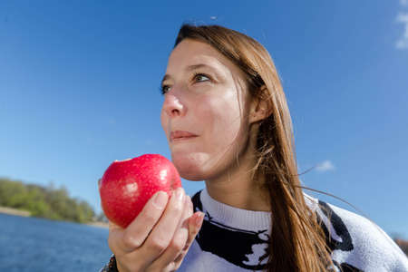 A young woman eating a healthy apple in the open air on a beautiful dayの写真素材