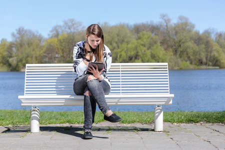 Young woman sitting with a tablet on a bench in the parkの写真素材