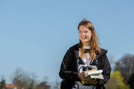 Woman with books laughs into the camera on a windy dayの写真素材