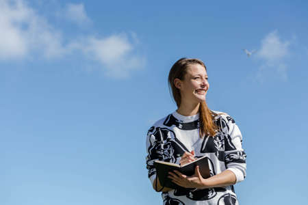 Young student is thinking and taking notes in a small book during nice weatherの写真素材