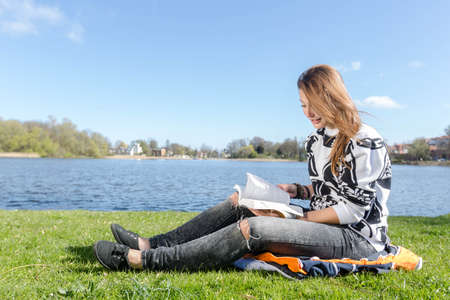 Girl reading and skimming through a book during nice weather in a parkの写真素材