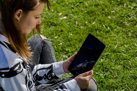 A young woman learns with a tablet in a park and looking at the screenの写真素材