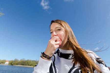 A young woman biting into a red apple and looking at the cameraの写真素材