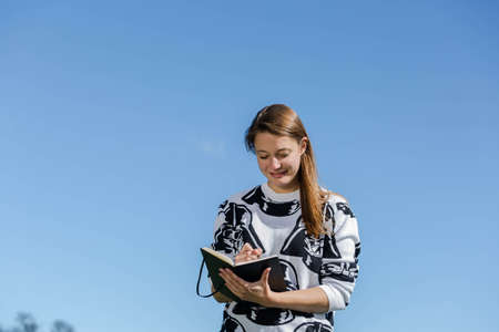 Student smiling during nice weather and taking notes in a bookの写真素材