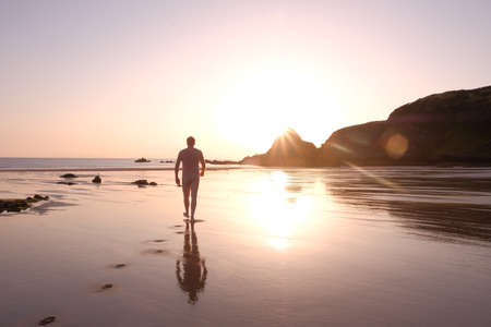 Figure strolls towards the sea across gleaming sand at sunriseの写真素材