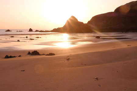 Sunrise on a golden beach with dramatic rocky coastline