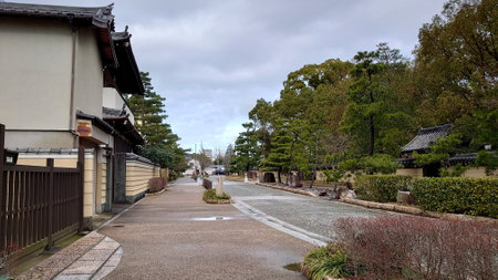 Fukuoka, Japan - 01.28.2020: An empty street in the Hakata temple town area with bushes and trees on the side along with traditional Japanese houses under a cloudy skyのeditorial素材