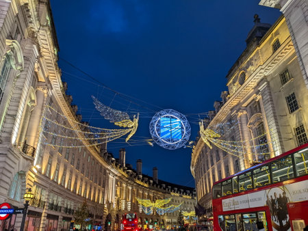 London, UK - 12.21.2021: Two angels Christmas lightings decorations hanging in the entrance of Regent Street with double-decker buses passing py under it during twilightのeditorial素材