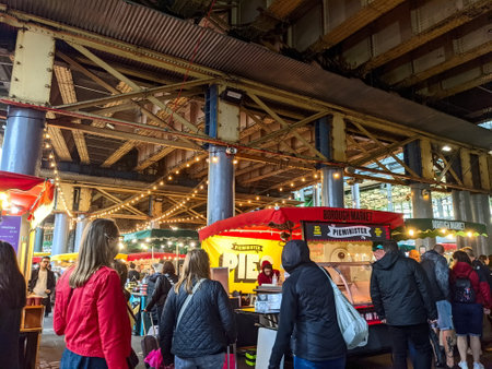 London, UK - 10.02.2021: Visitors walking past a pie stall alongside other vendors under a railway viaduct in the bustling Borough Market during the pandemic in the daytimeのeditorial素材