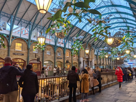 London, UK - 11.05.2021: Visitors standing next to the railings, looking down to a restaurant seating area in the Greco-Roman style Covent Garden market under a curved glass ceiling during duskのeditorial素材