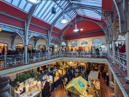 London, UK - 11.27.2021: Customers walking between craft stalls in an atrium of Camden Lock Market with customers browsing shops upstairs and sunlight coming through a glass ceilingのeditorial素材