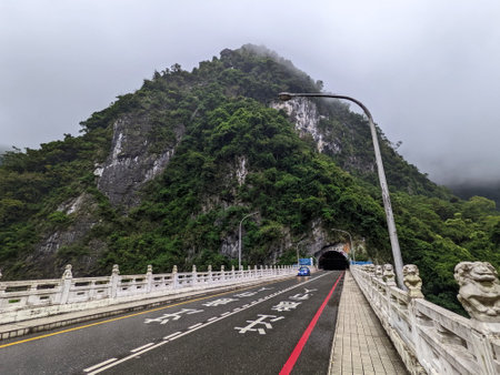 Taroko, Taiwan - 11.26.2022: A car driving on the Shakadang Bridge next to the entrance to the Shakadang Trail after leaving the Shakadang Tunnel with a foggy mountain at the back during the pandemicのeditorial素材
