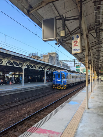 Tainan, Taiwan - 12.02.2022: A blue local train approaching Tainan Station platform 1 with passengers waiting on the platform under a blue sky during the pandemicのeditorial素材