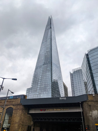 London, UK - 07.07.2022: The Shard together with other modern glass buildings standing behind the London Bridge Station with a train passing on the bridge on a cloudy day during the pandemicのeditorial素材
