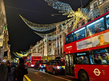 Iconic red double decker buses driving past angel Christmas lights on Regent Street in Londonのeditorial素材