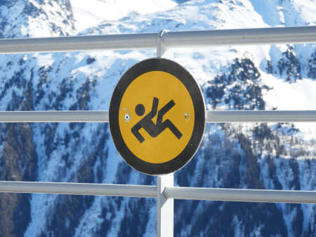 yellow and black sign on railing with mountains covered with snow at the backの写真素材