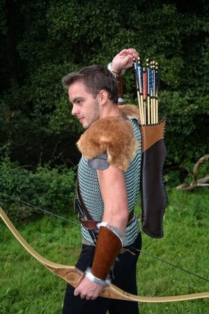 Young Medieval archer with chain shirt Reaches for arrow, with bow in hand in nature