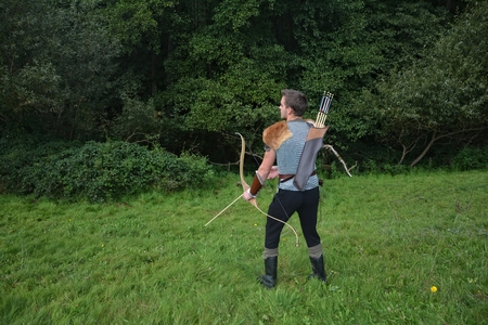 Young medieval archer with chain shirt, bow and arrow in nature during sheet tensioningの写真素材