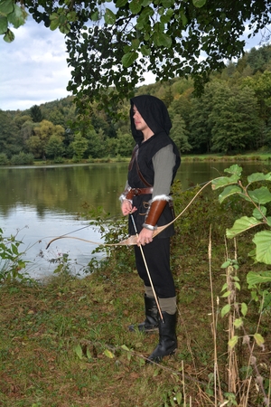 Medieval archer with black hood stands with tense curve and with arrows in the lakeの写真素材