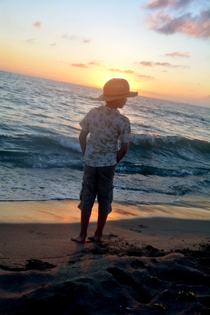Small boy stands on the beach at the sundown, hands in the trouser pockets and looks asideの写真素材