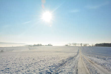 Snow-covered road in winter in the countryside with sun in Spessart, Bavaria, Germanyの写真素材