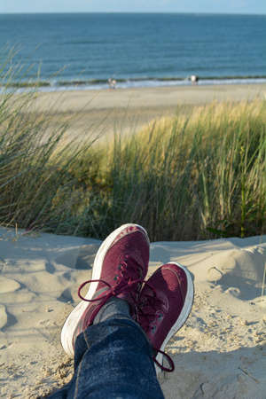 Resting between the dunes, lying on the beach with sneakers, with a view of the sea on the North Sea coast in the Netherlandsの写真素材