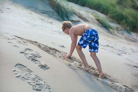 Boy climbs up a sand dune in summertimeの写真素材