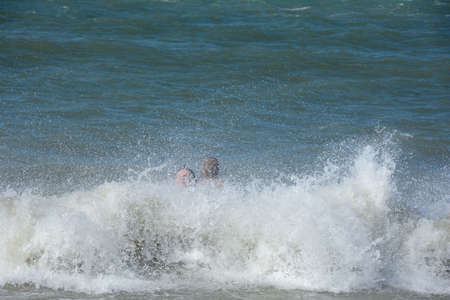 Two children sit happily in the middle of a splashing wave by the sea, on the North Sea coast in the...