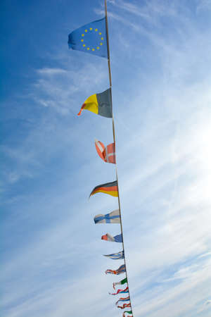 Flags from several different countries hang from a rope, against a lot of blue sky