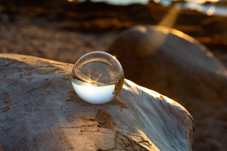 Glass ball on a rock at sunset on the beach, the sea and the setting sun are reflected in the ballの写真素材