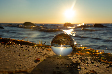A glass ball lies in the sand in front of the waves, beach with algae and the sea and the setting...