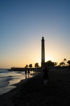 Lighthouse in Maspalomas ( Faro de Maspalomas ) on the Canary Island of Gran Canaria in Spain at sunset with a girl,sandy beach and seaの写真素材