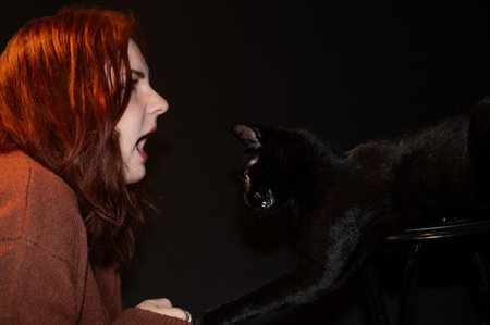 A red-haired girl with her black cat and black backgroundの写真素材
