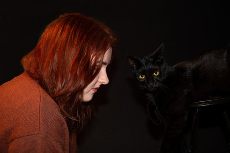 A red-haired girl with her black cat and black backgroundの写真素材