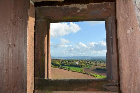 View through an old castle window on a blue sky with white clouds and green landscapeの写真素材
