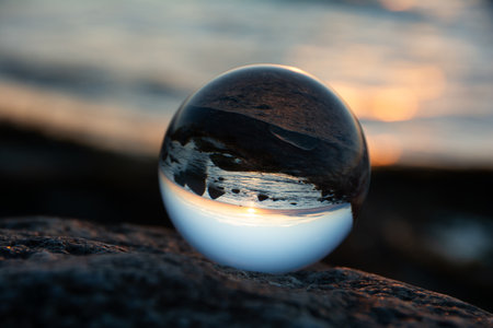 Glass ball on a rock at sunset on the beach, the sea and the setting sun are reflected in the ball