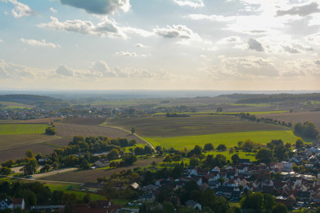 Top view of a green landscape with houses of a village, farmland, forest and blue sky
