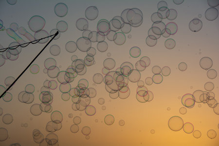 Lots of colorful soap bubbles floating in the orange sky at sunset with soap bubble stick