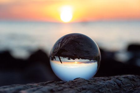 Glass ball on a branch  at sunset on the beach, the sea and the setting sun are reflected in the...