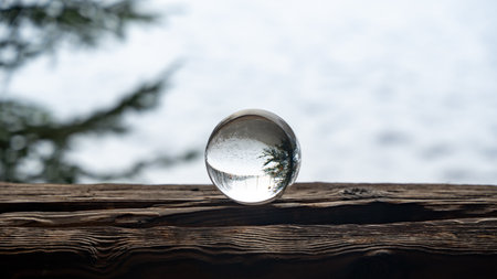 Glass ball on a wood on a cold winter day, with reflections of trees and snow in the glassの写真素材