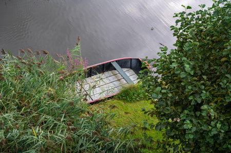 Small boat lies in the water, on the bank of a riverの写真素材