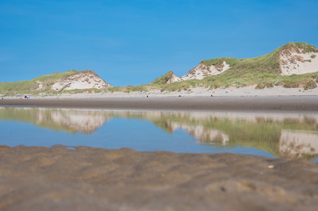 Sand dunes are reflected in the still, standing water at low tide at seaの写真素材