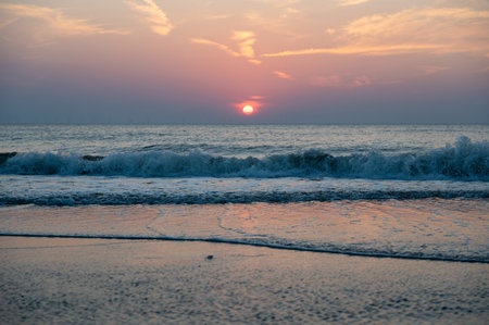 Sunset with red sun over the sea, with waves and sandy beach