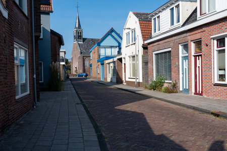 A small street in the town of Egmond aan Zee in the Netherlands, overlooking a church with blue skyの写真素材