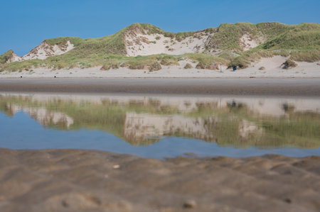 Sand dunes are reflected in the still, standing water at low tide at seaの写真素材